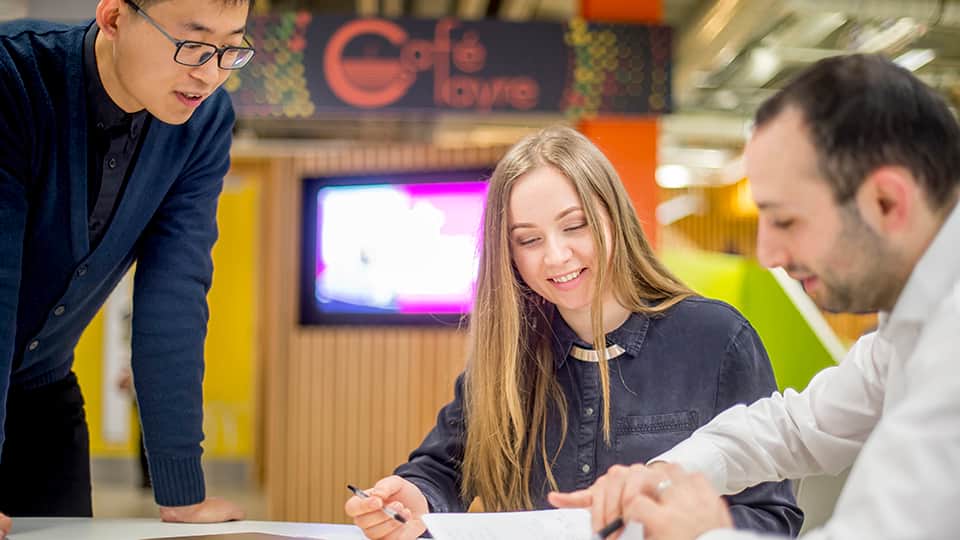 three people talking, two are seated at a table