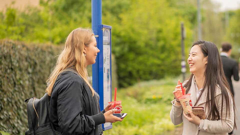 two students standing at a bus stop talking