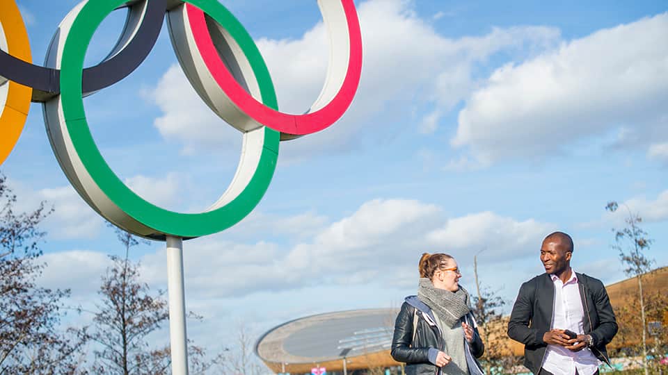 two people walking past a sculpture of the Olympic rings