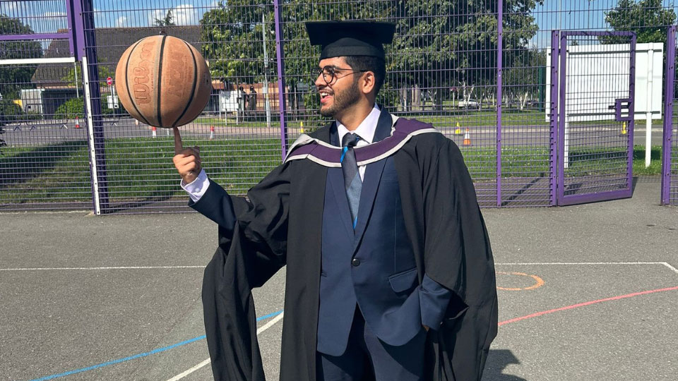 Kumaran wearing a graduation gown and holding a basketball