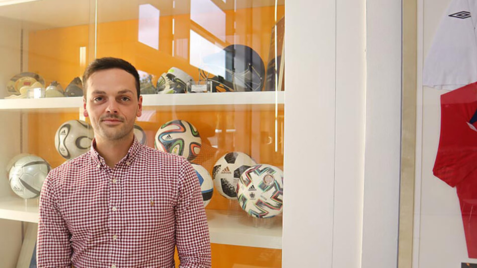 Dr Jon Farmer stood in front of a cabinet of sports equipment