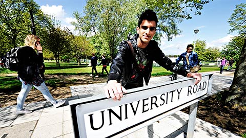 Student leaning on University Road sign