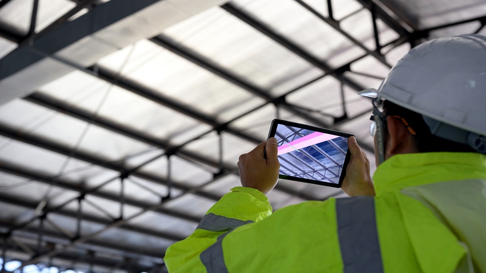 A construction worker looks at a roof with an iPad