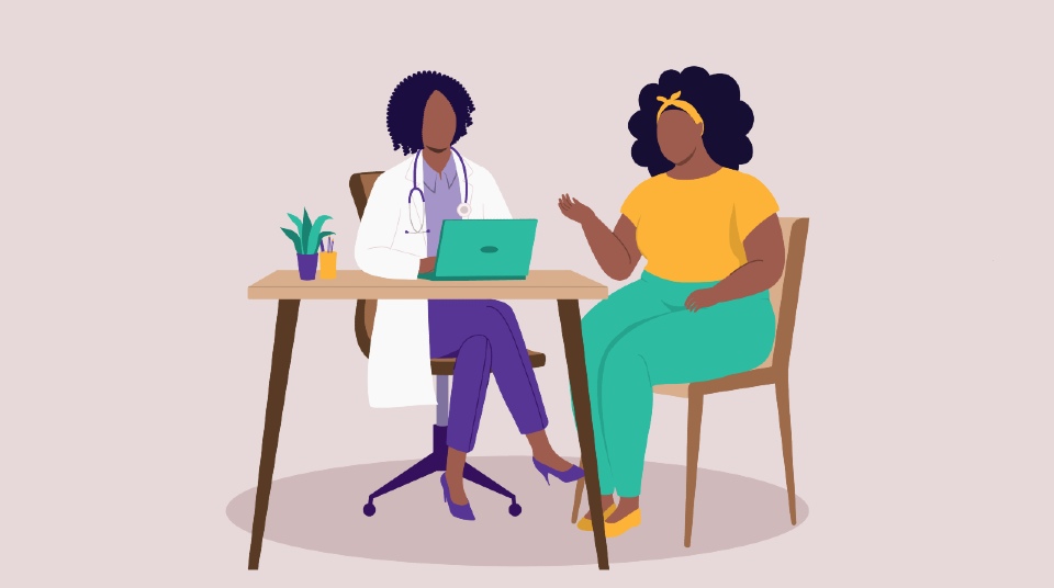 A woman in a yellow top and green trousers sat across from a doctor in a white lab coat behind a desk with a green laptop open