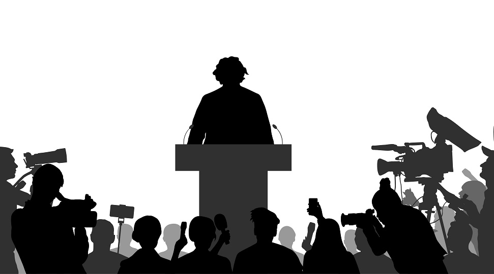 An Election Candidate on a podium with election program surrounded by reporters and cameramen. Silhouette of people.