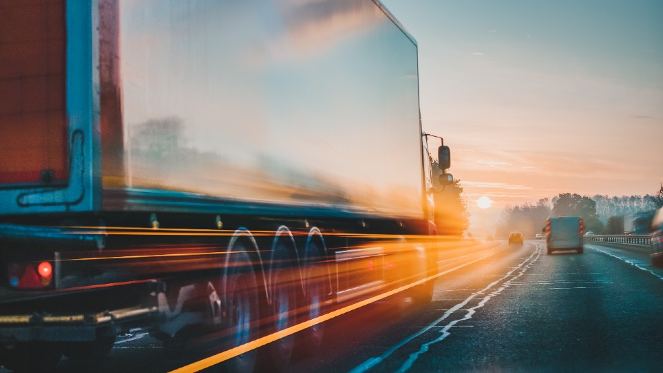 A white HGV driving on the motorway, it has a blur effect on it, making it look like it is moving fast.