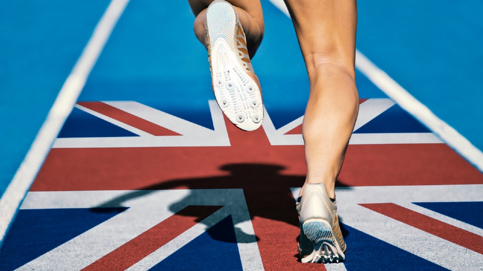 Picture of a track runner sprinting across a GB flag printed on the floor of a blue running track