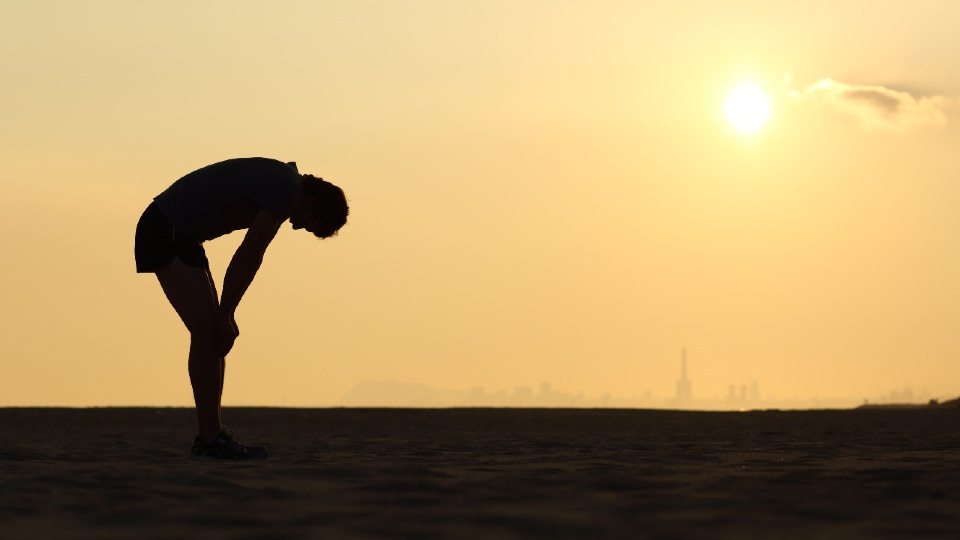 the silhouette of a runner bent over, indicating they are tired