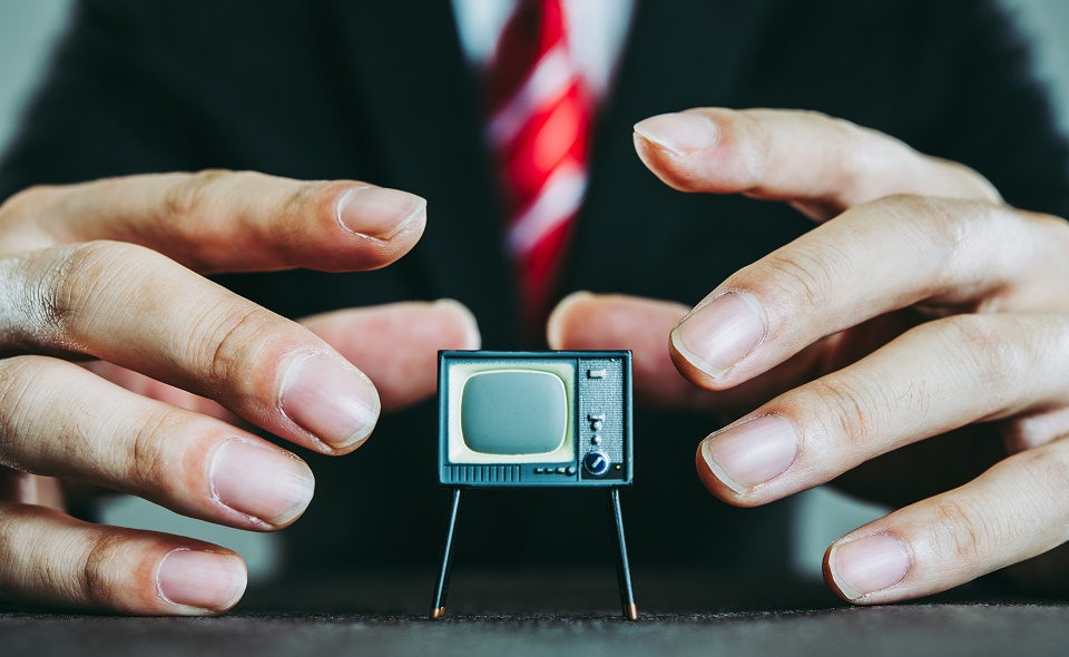 A man in a suit has his hands ready to pick up a miniature television set.