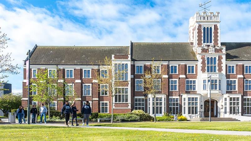 A group of students are walking past the Hazelrigg Building on the Loughborough University campus.
