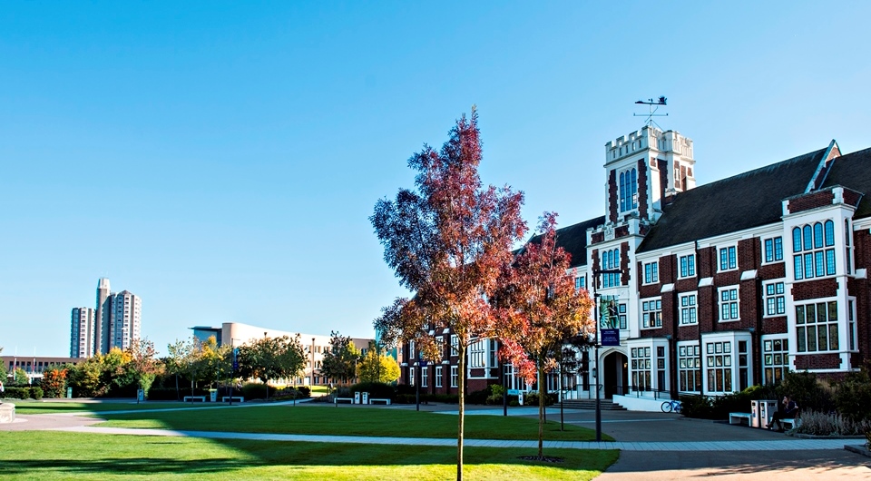The Hazelrigg Building with a bright blue sky behind a tree in front with autumnal orange leaves