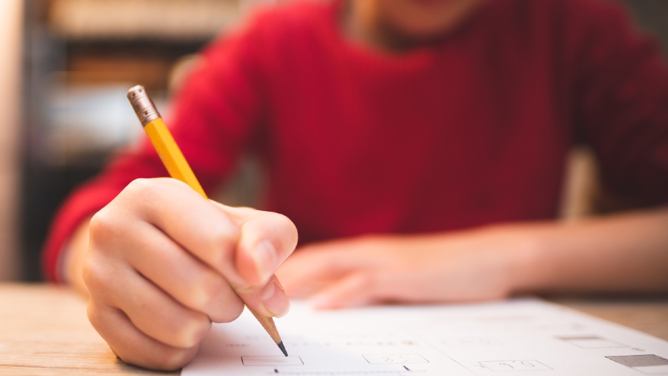 A child in a red top with a pencil working on a piece of paper
