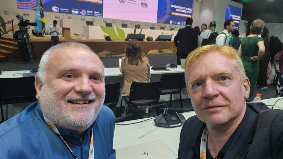 Two men look into the camera with a crowd behind them