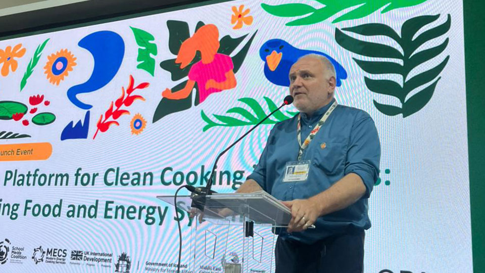 A man talking at a podium with a large display on a screen behind him
