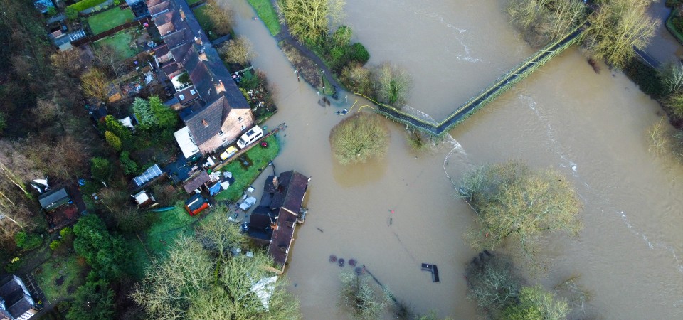 An aerial shot of a flooded village. Water is raised covering roads, fields and hedges.