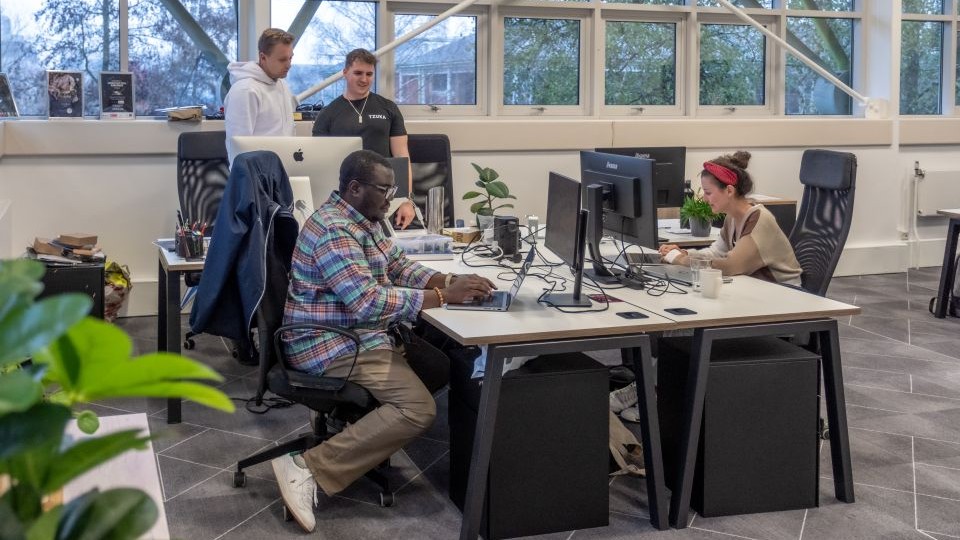 A group of student entrepreneurs are sat around desks, working on laptops and sharing ideas.