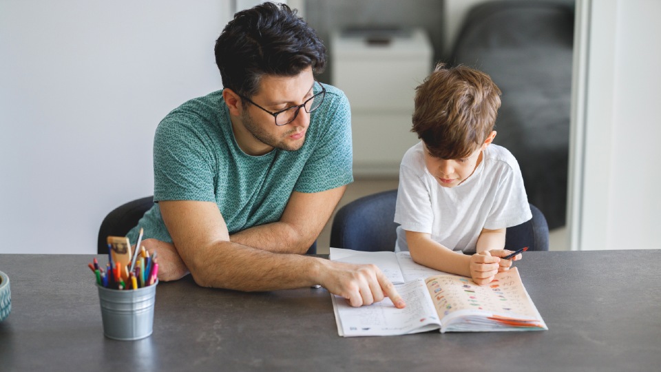 A father and son sat looking at homework at a grey desk