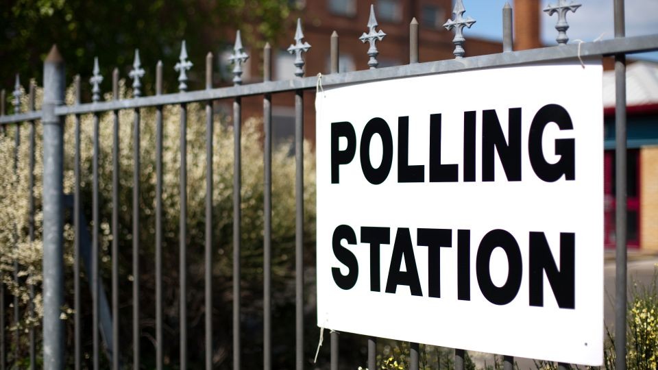 A white sign with black lettering attached to some railings which says 'Polling Station'