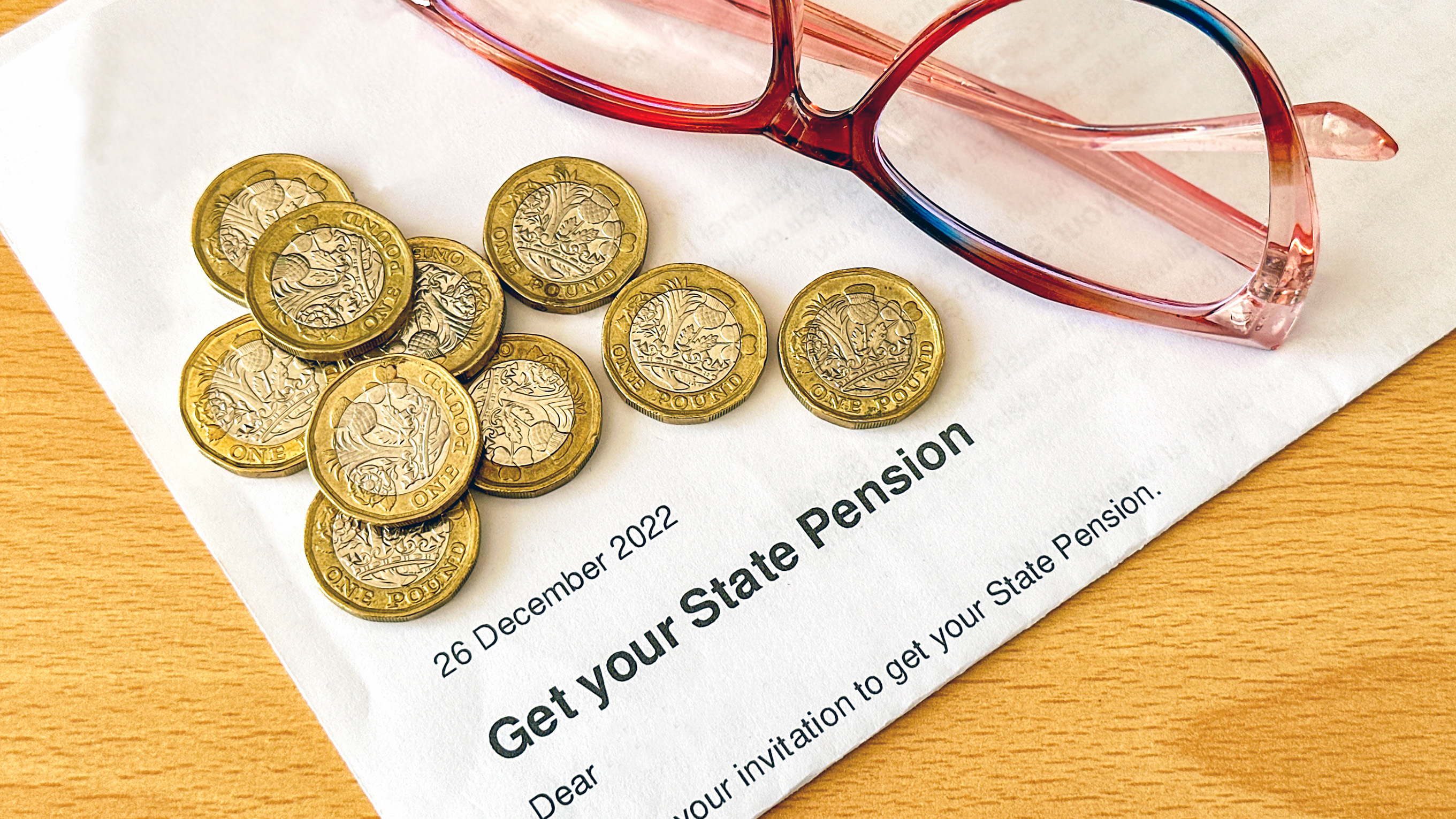 letter to claim state pension, pound coins and glasses on table