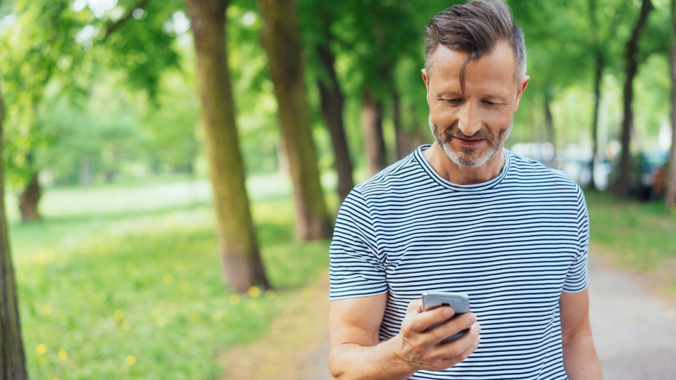 A middle aged man looks at his phone while taking a walk