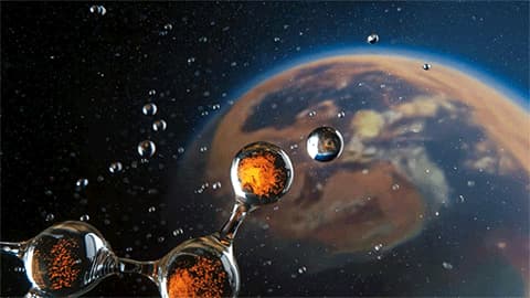 The image shows water droplets in a low-gravity environment, likely space, with a blurred image of Earth in the background.