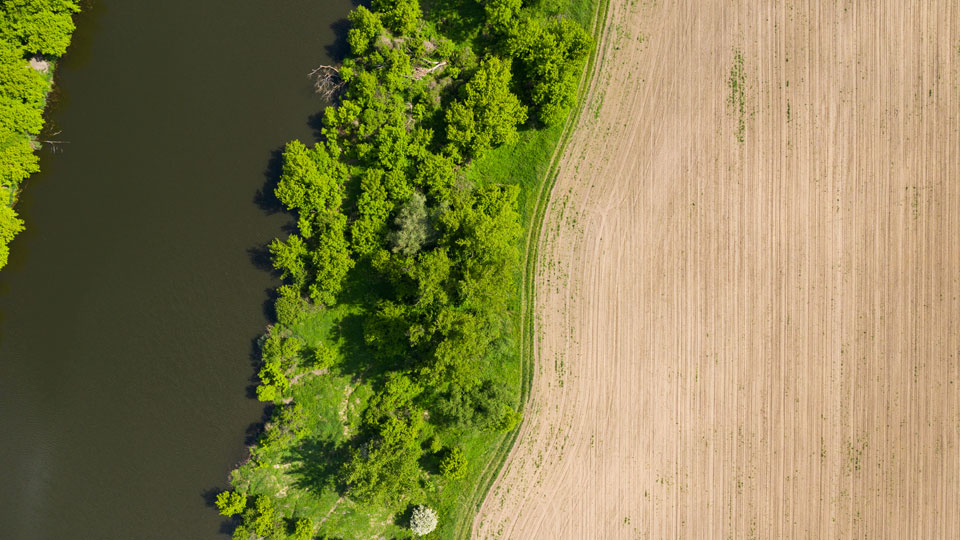 Aerial photograph showing a bend in a river - hemmed by woodland and a ploughed field.