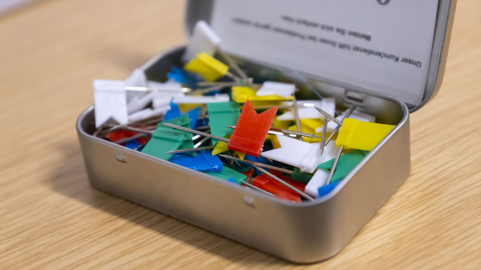 An open tin, full of flag pins - used to pinpoint locations on a map