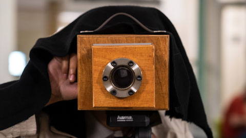 Scientist demonstrating how a pinhole camera works. The lens is focused out of the photograph straight towards us - smile, please!