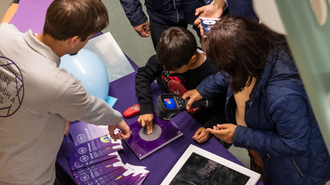 Taken from above, looking down on the subjects - a scientist works with a family group to explore infrared imaging
