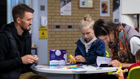 A family with two young children - sitting at a table, exploring some of the exhibition activities
