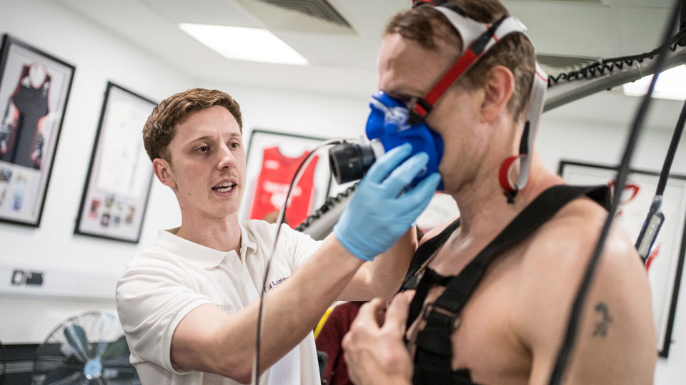 Researcher fitting a respiration monitor to the face of a Para athlete who is on a treadmill