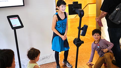 A child standing facing a tripod-mounted tablet computer with a camera attached to it