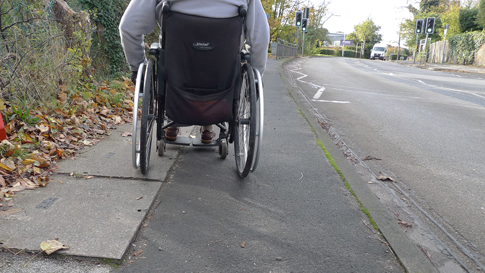 Wheelchair user on pavement trying to navigate uneven surfaces in their chair.