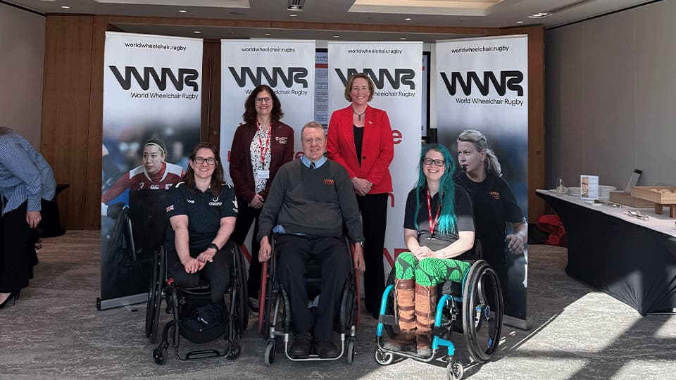 A group of 5 people, including three wheel-chair users in front of WWR banners