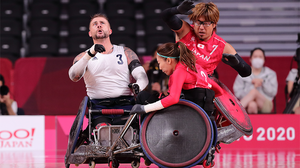 three wheelchair rugby athletes (2 male and 1 female) competing for the ball at a wheelchair rugby competition