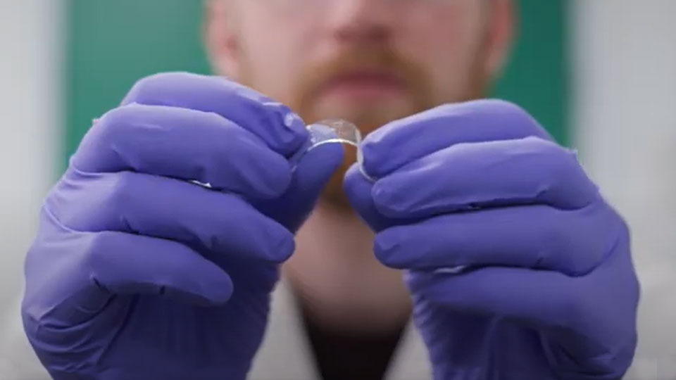 Close-up shot of a piece of the new material held between the blue-gloved fingers of a researcher