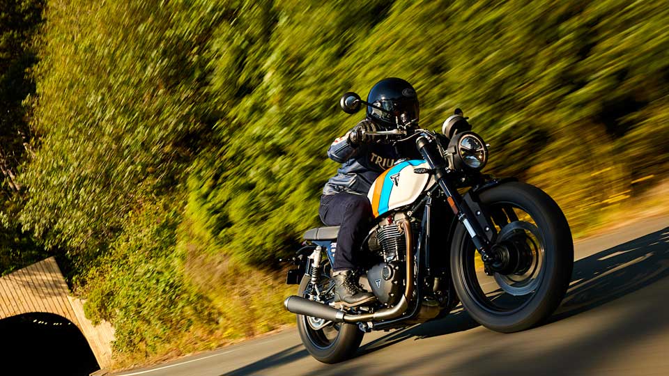 A motorbike travelling at speed (left to right), leaving a tunnel along a tree-lined road
