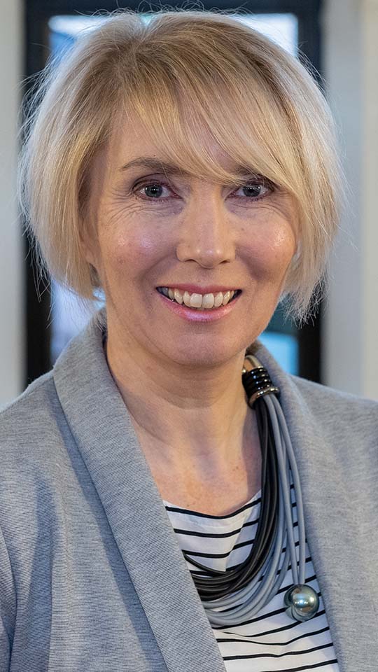 A portrait photo of Lizzie Gadd standing against a stained glass window
