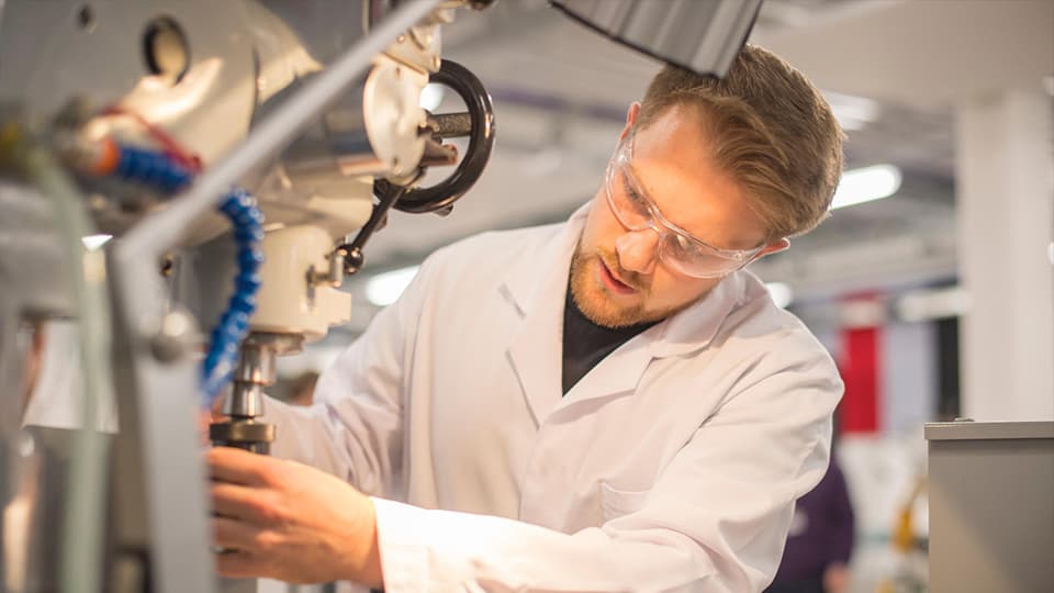 male student working in lab wearing lab coat and goggles