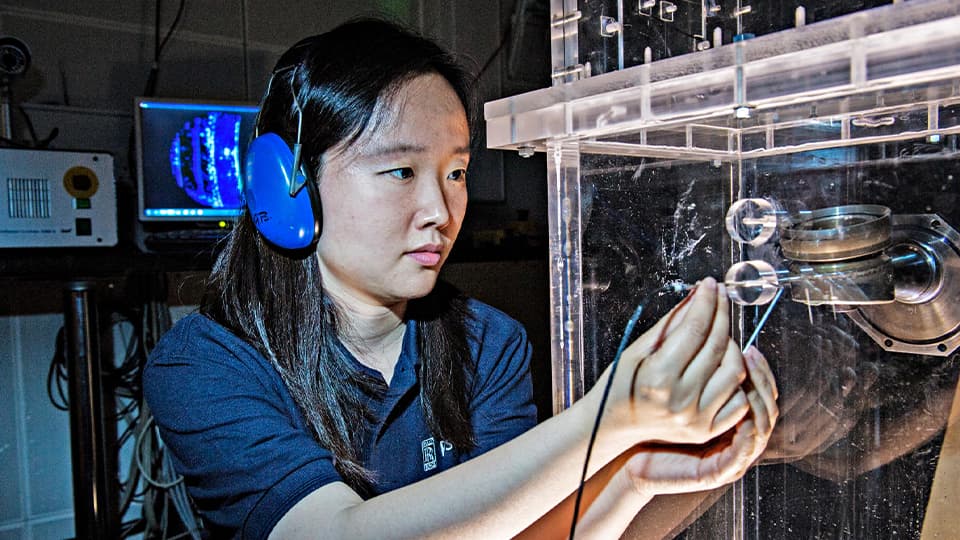 female with ear defenders on holding a metal pin to a machine for research