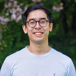 Male student wearing glasses and a grey t-shirt with a blossoming tree in the background