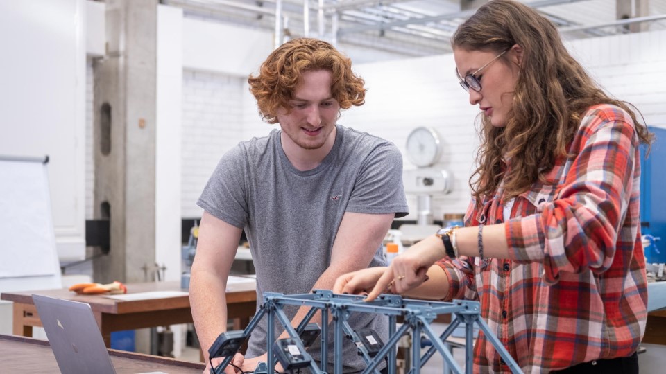 A male and female student building a small table top bridge