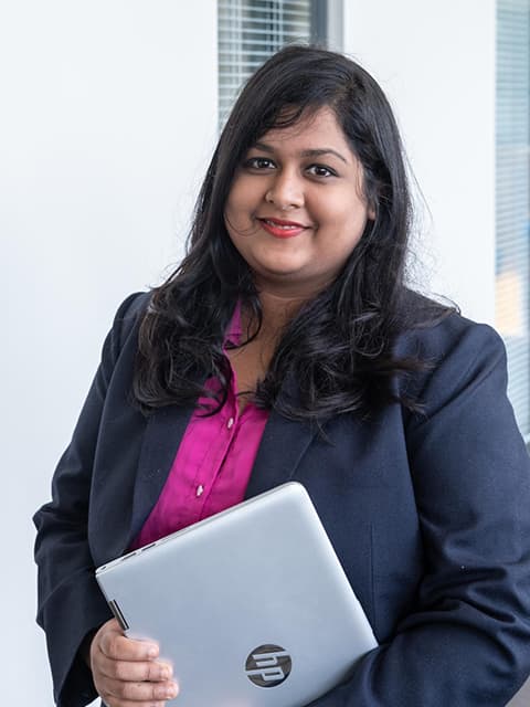 An MBA student smiling towards camera holding a laptop.