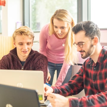 Three people huddled around a laptop