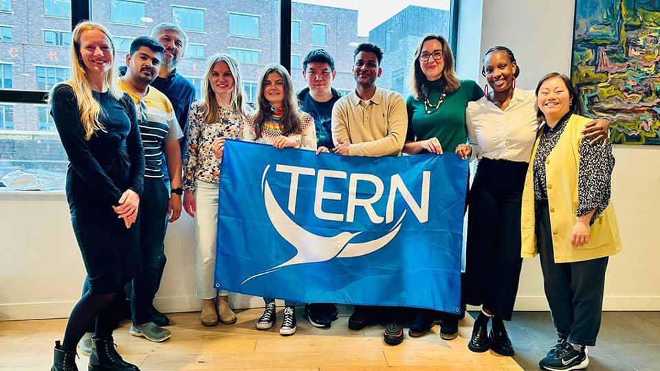 A group of people stood in a row, holding a large blue flag with the TERN logo.
