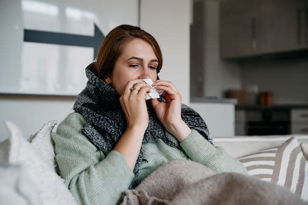 A person on a sofa coughing/sneezing into a tissue.