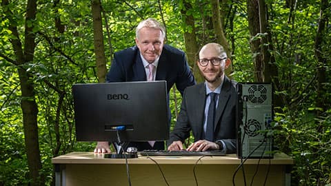 Professors Tom Jackson and Ian Hodgkinson in a woodland setting, using a desktop computer.