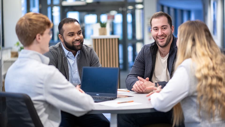 A group of four students sitting round a table chatting and laughing.
