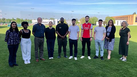 Professor Jeffrey Wooldridge with staff and students from Loughborough Business School standing outside on a green field.