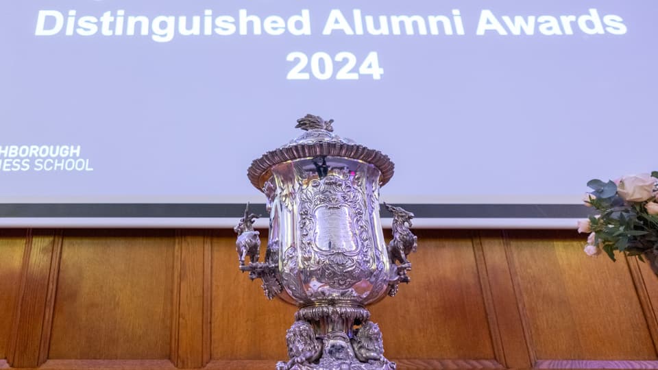 A trophy in front of a screen that reads 'Distinguished Alumni Awards 2024'.
